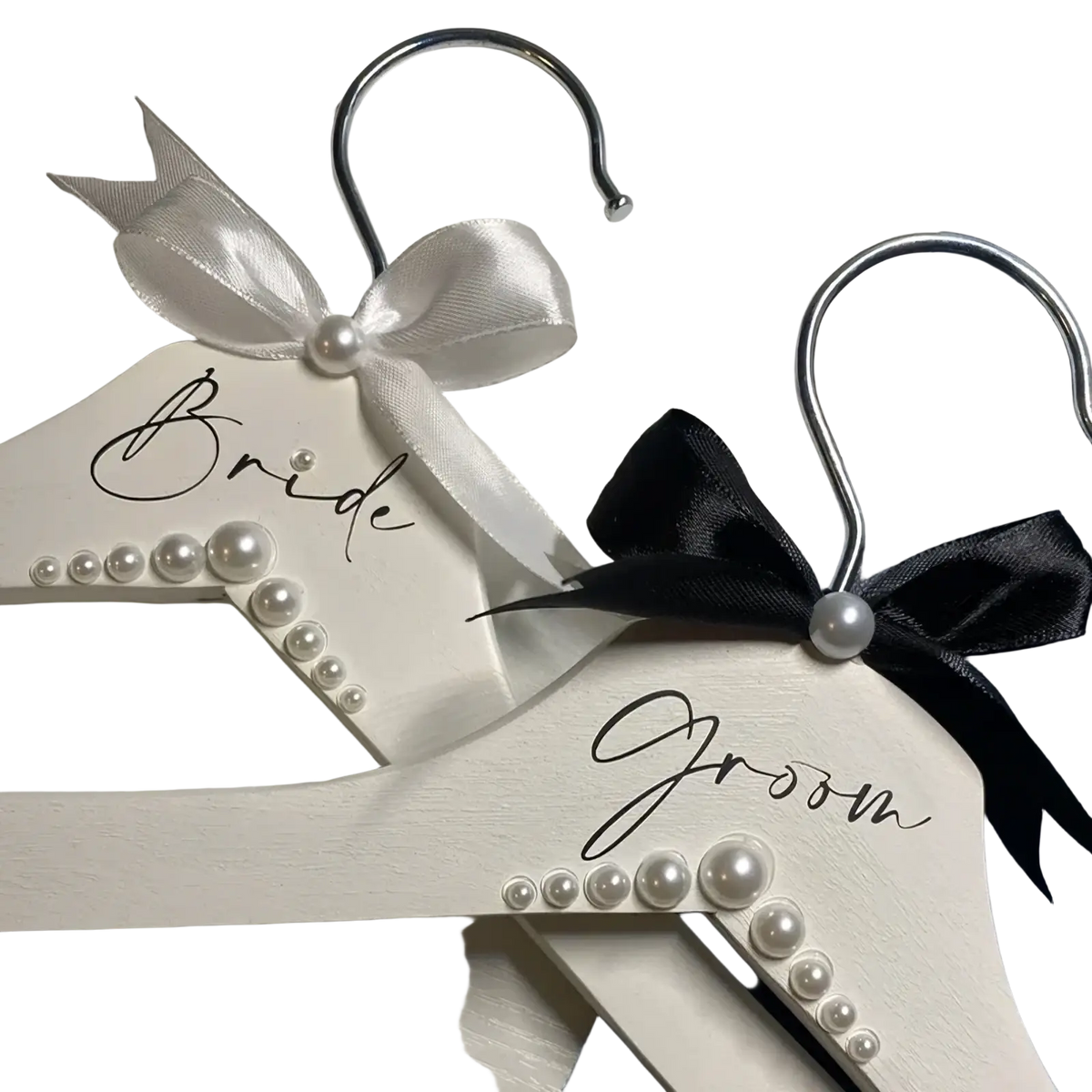 White wooden wedding hangers set with pearls satin bows one labeled bride in black cursive for bride and groom use