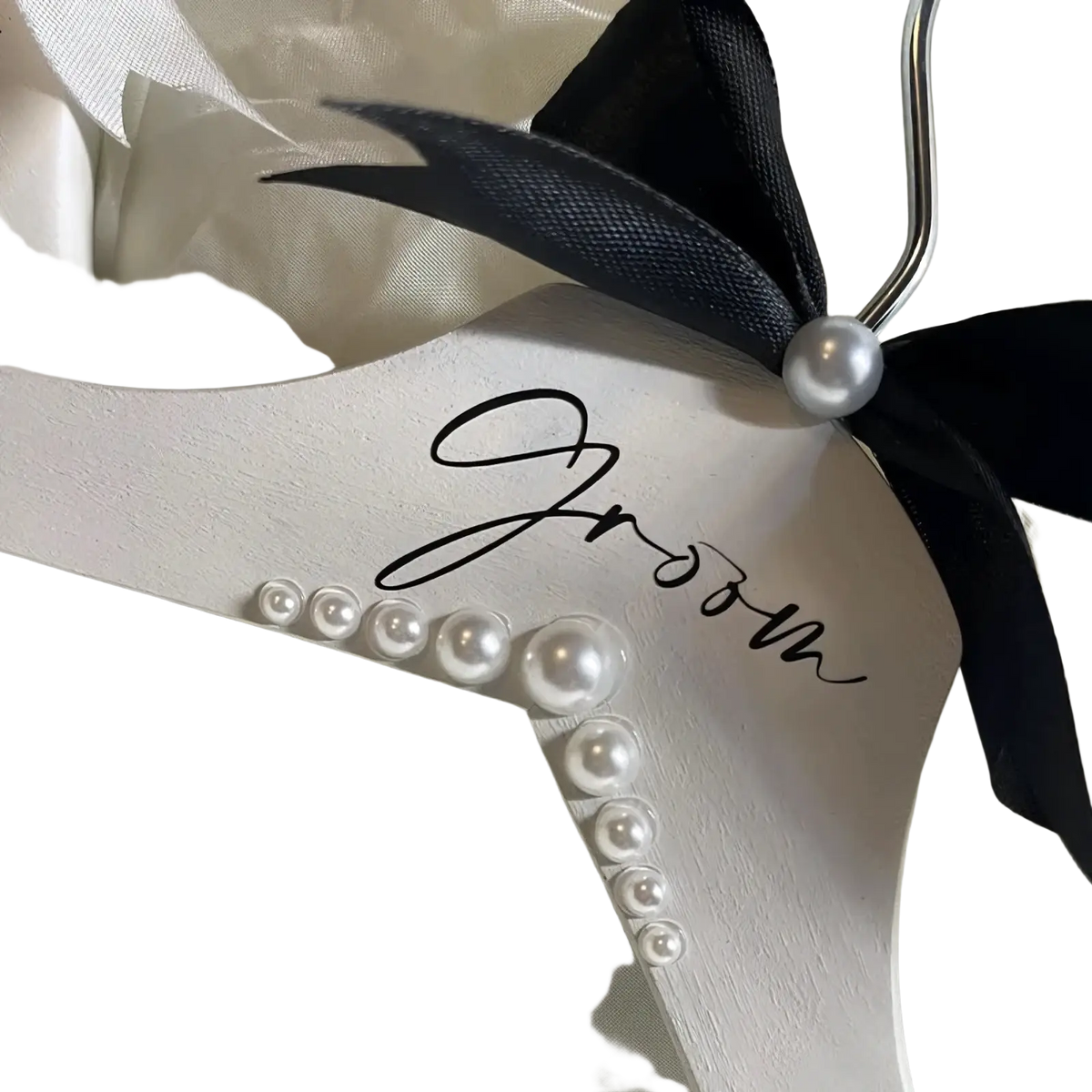 White wooden groom hanger with black ribbon bow, pearl accent, and cursive lettering adorned with graduated pearls