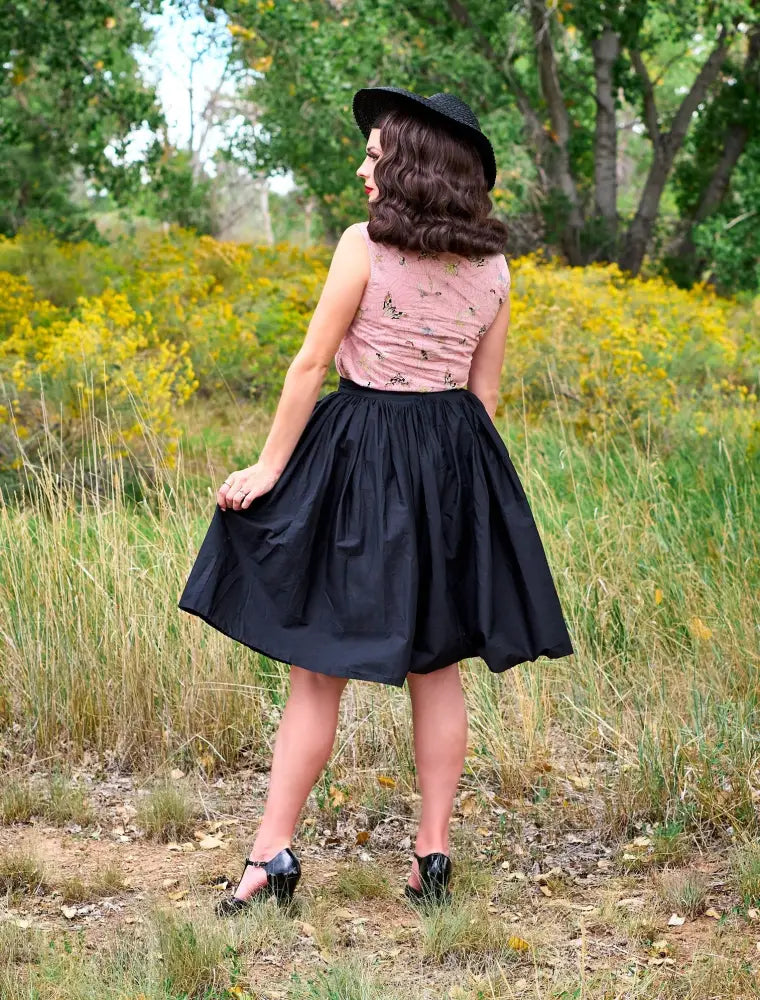 Black pleated 1950s cotton swing skirt with pockets paired with a fitted pink floral top and black hat