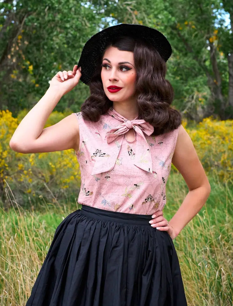 Pink sleeveless blouse with delicate floral pattern and bow paired with peggy black 1950s cotton swing skirt with pockets