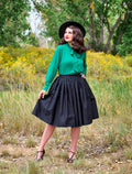 A woman wears a black Peggy black 1950s cotton swing skirt with pockets paired with a green blouse with a bow neckline