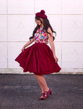 A woman wearing a vibrant floral top with a rich burgundy Peggy cotton 1950s swing skirt with pockets and beret