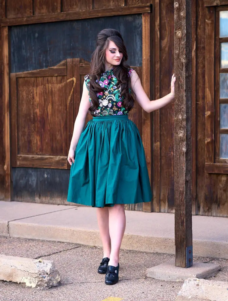 A woman wears a sleeveless embroidered floral top paired with a green cotton Peggy Green 1950s swing skirt with pockets