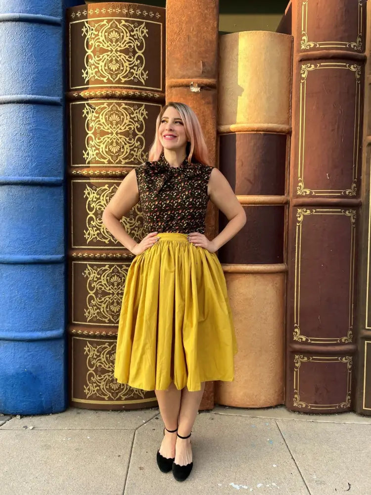 A woman wearing a Peggy mustard yellow 1950s cotton swing skirt with pockets and a black lace top