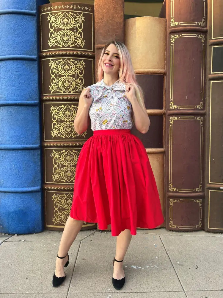 A woman wearing a white blouse with gold floral patterns and a red cotton midi Peggy swing skirt with pockets