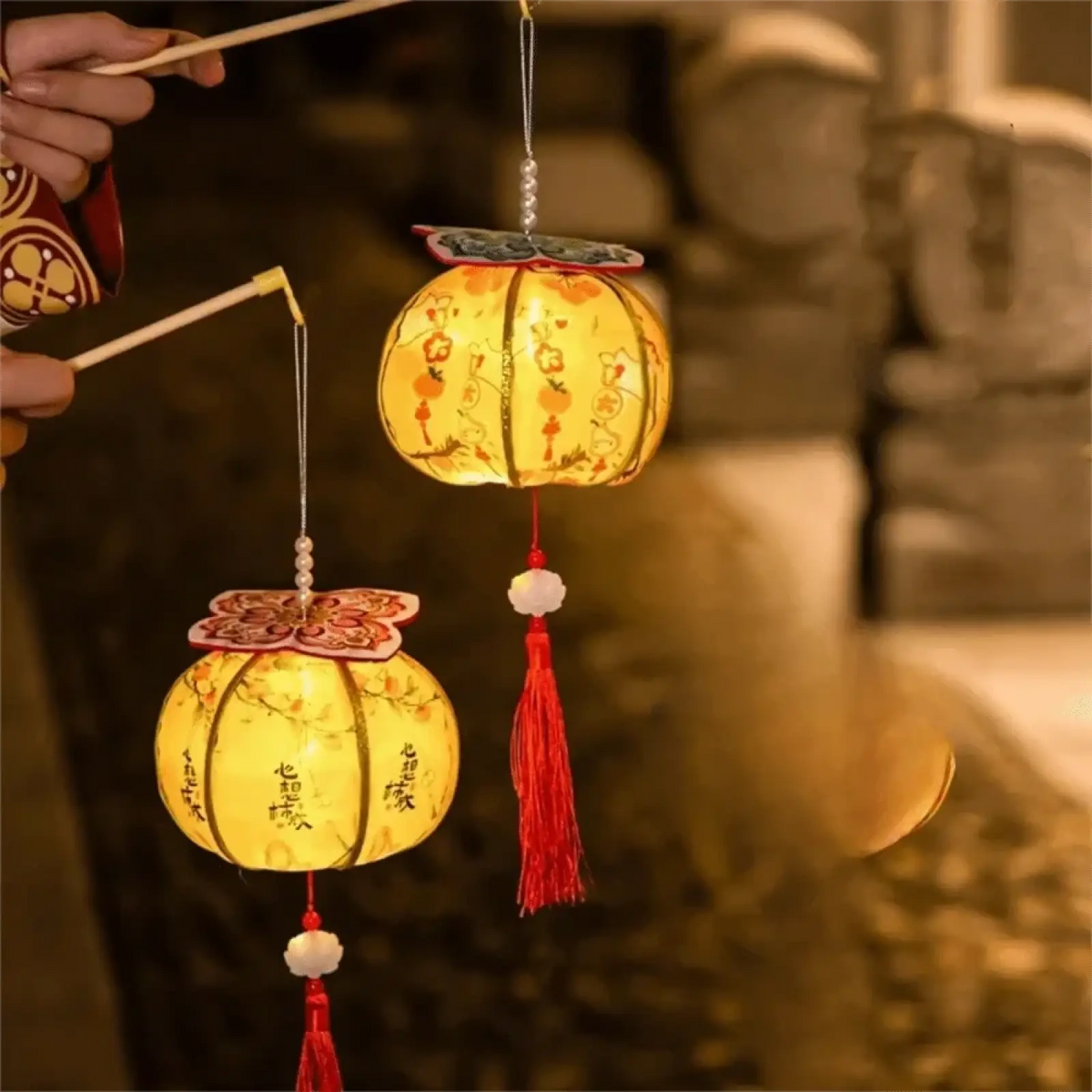 Two glowing yellow persimmon lanterns with floral designs and red tassels for chinese new year led decor