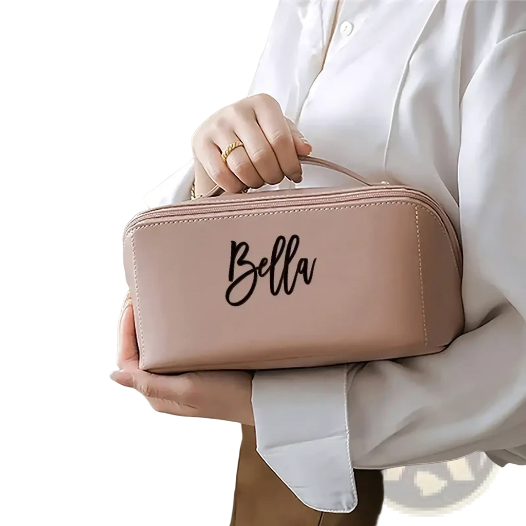 A soft blush pink faux leather personalised makeup bag with black cursive bella engraving and top handle