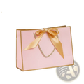 A pink personalized bridesmaid gift bag with gold trim and satin ribbon bow for custom name presentation
