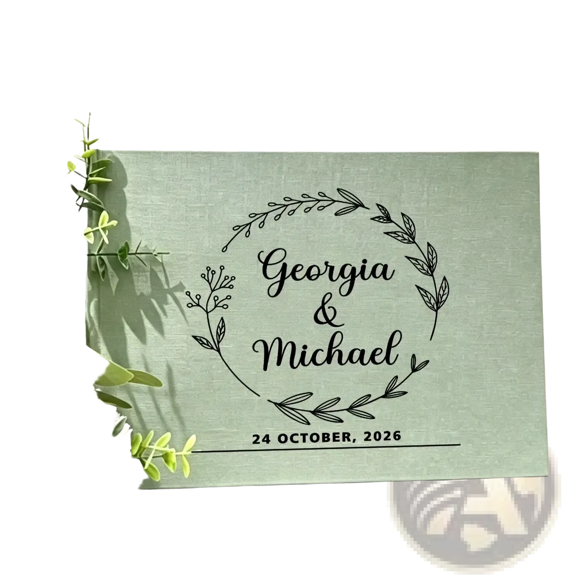 A mint green linen wedding guest book with black engraved floral wreath and personalized names and wedding date