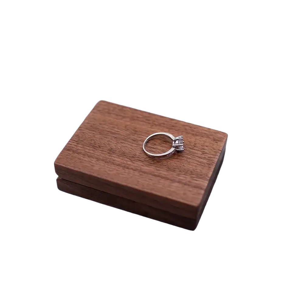A silver engagement ring with diamonds resting on a personalized walnut wood wedding ring display box