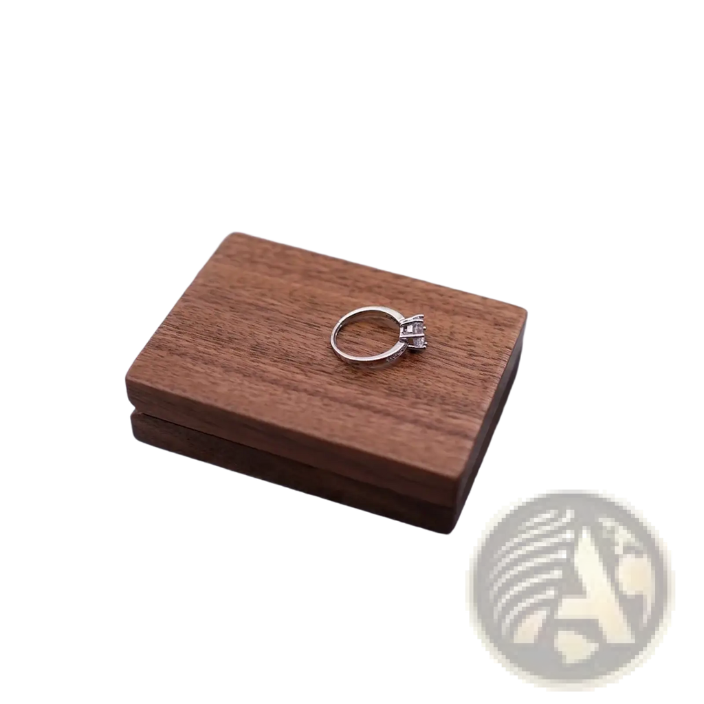 A silver engagement ring with diamonds resting on a personalized walnut wood wedding ring display box