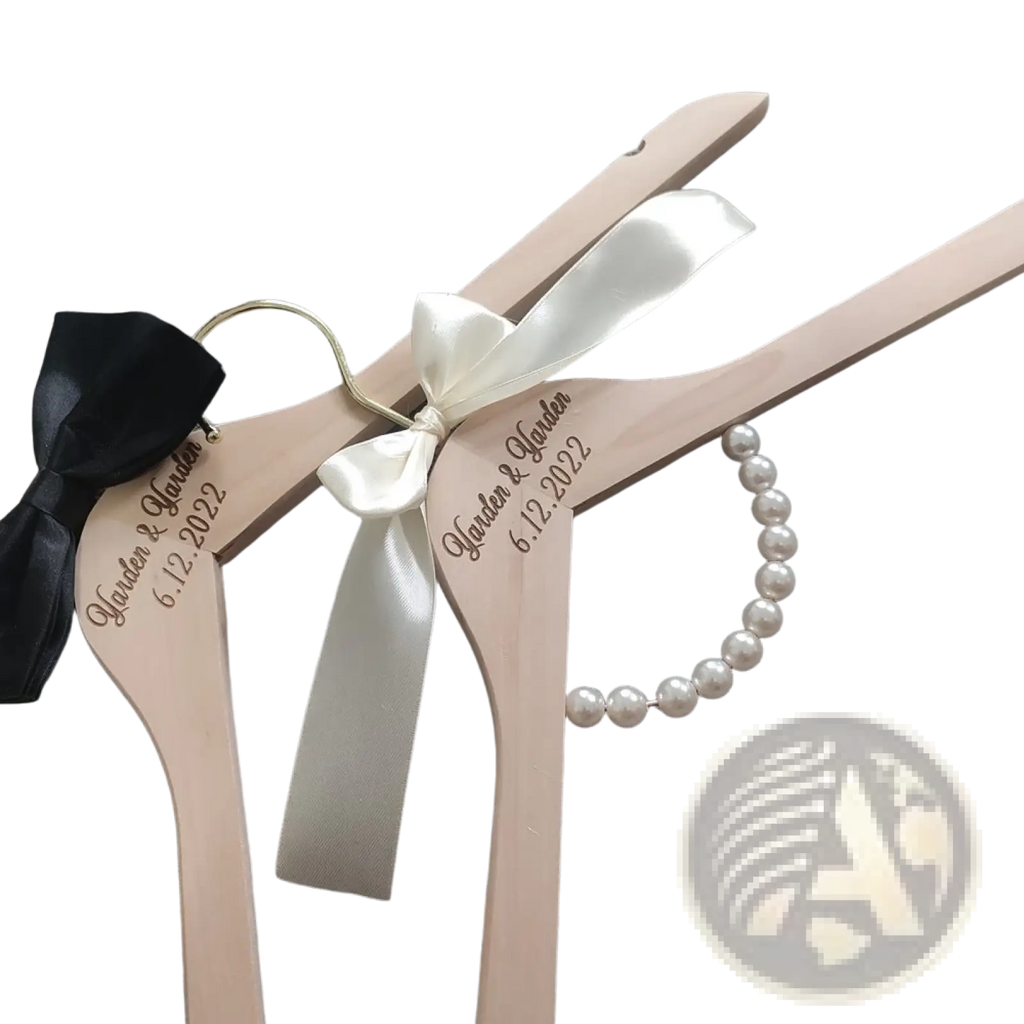 Light pink wooden wedding hangers with custom engraved names and date adorned with satin ribbons and pearl bracelets