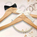 Light wood personalized wedding dress hangers engraved with names and date adorned with black and white satin bows