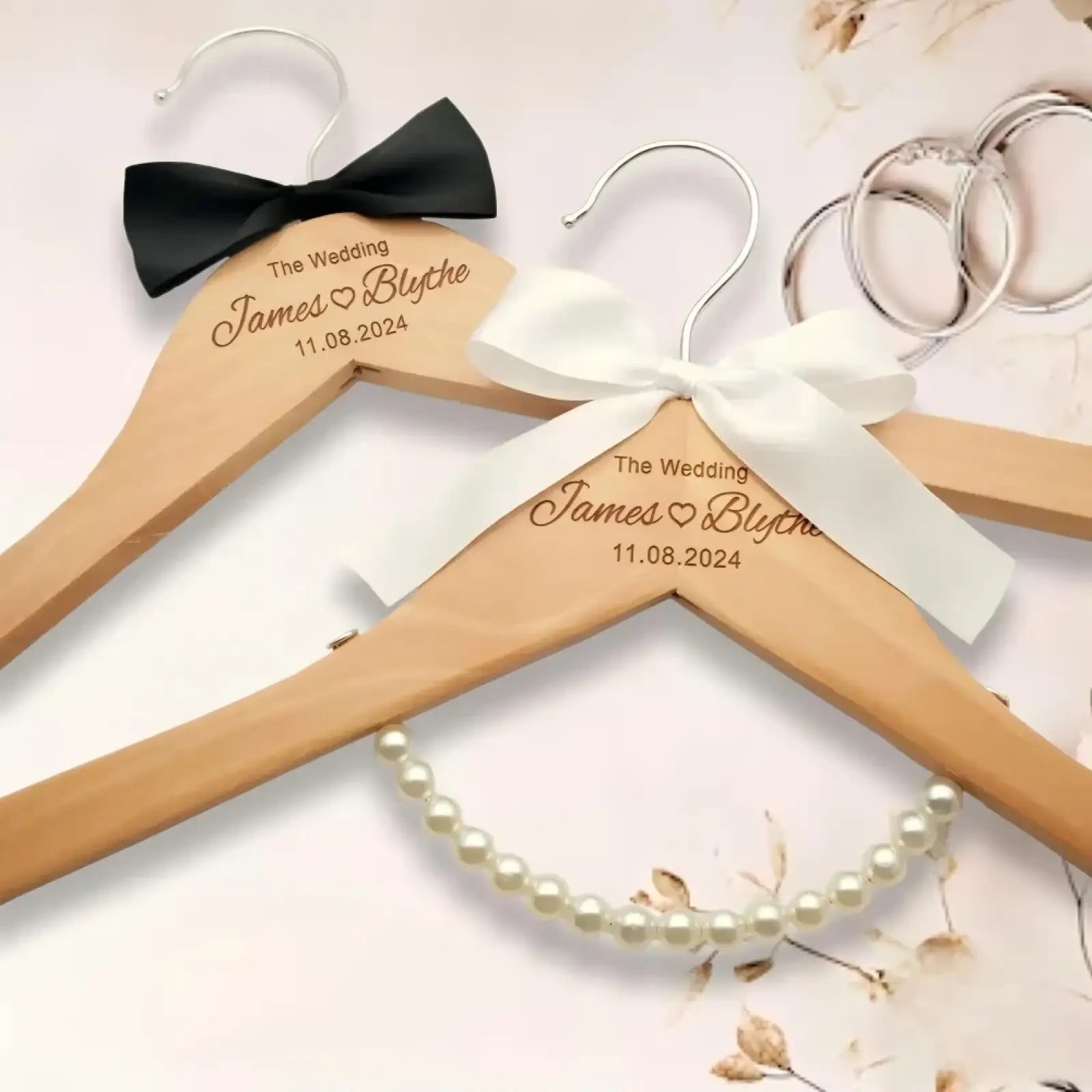 Light wood personalized wedding dress hangers engraved with names and date adorned with black and white satin bows