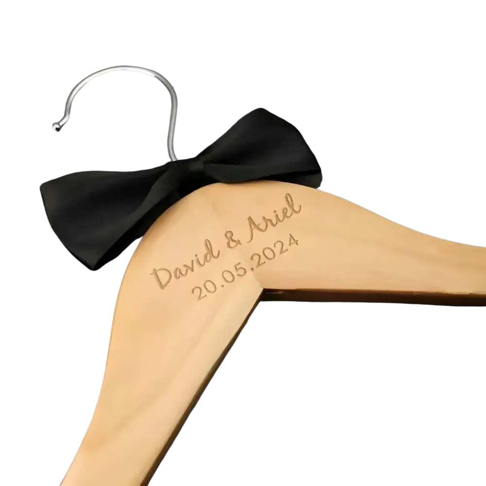 Light-colored wooden personalized wedding dress hanger with engraved names and date adorned with black satin bow
