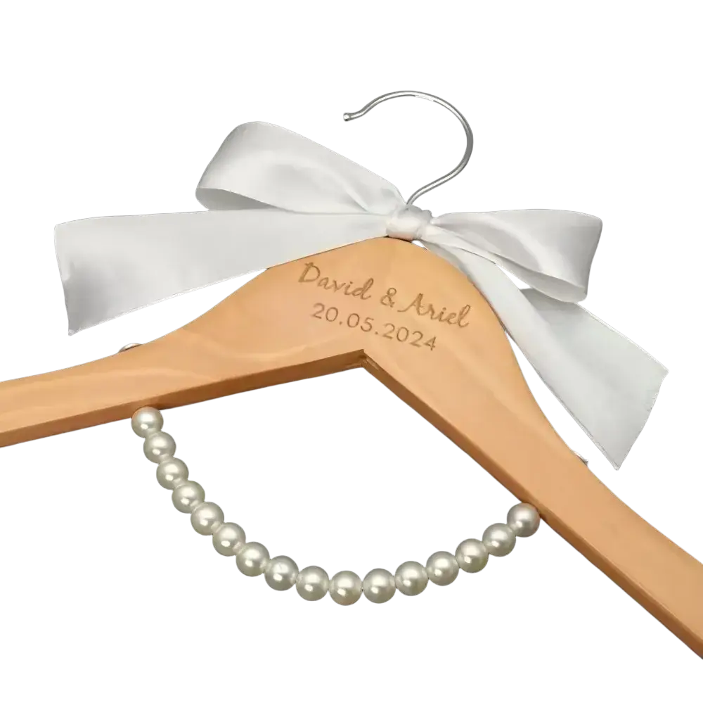 A light wood personalized wedding dress hanger engraved with names and date and a white satin bow bridal gift