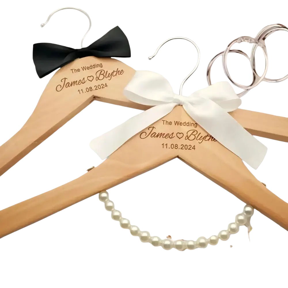 Light wood personalized wedding dress hangers engraved with names and date adorned with black and white satin bows