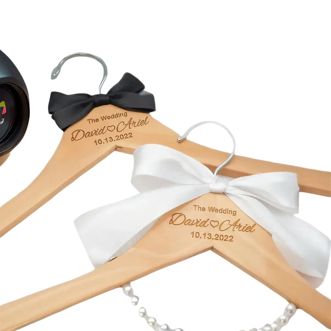 Light-colored wooden wedding dress hangers engraved with names and date featuring black and white bows in personalized set
