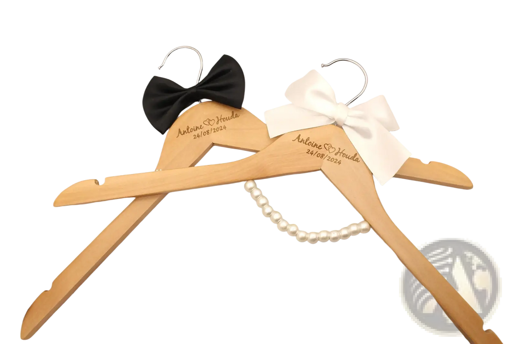 Two light wood personalized wedding dress hangers engraved with names and date, adorned with black and white bows