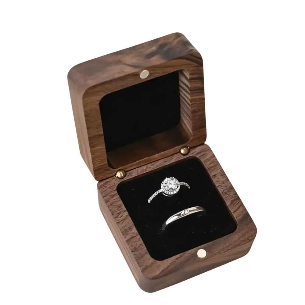 A personalized wooden wedding ring box in dark wood with a black velvet interior holding an engagement ring and band
