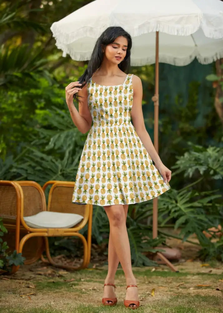 A woman wearing a white pineapple print sleeveless a-line skater dress with pockets in a casual style
