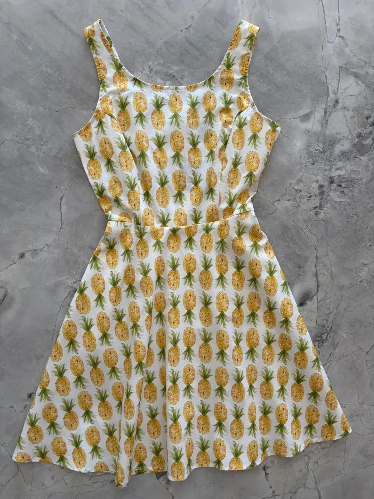 White pineapple print sleeveless skater dress with pockets featuring a yellow pineapple pattern on a white fabric