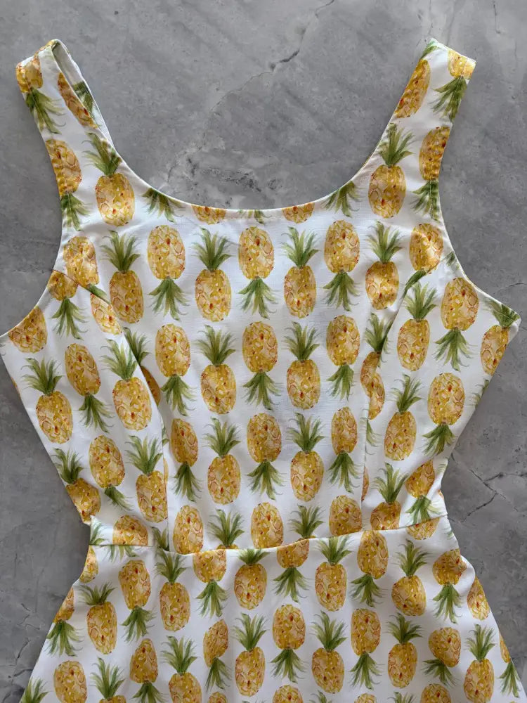 White pineapple print sleeveless skater dress with pockets featuring a repeating pattern of yellow pineapples and green tops