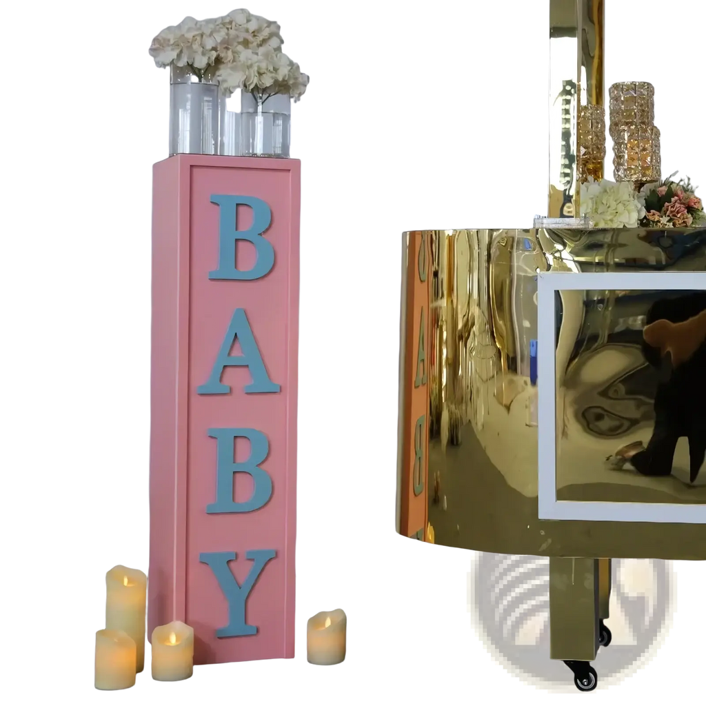 Pink baby shower balloon box decoration featuring a pink rectangular pillar with light blue 3d baby letters and white flowers