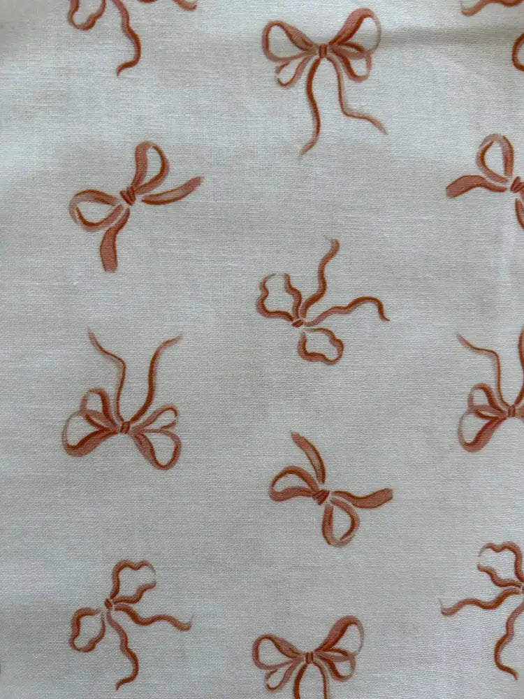 Cream-colored sleeveless cotton blouse with rust-brown bow pattern featuring a neckline bow for a retro pink look