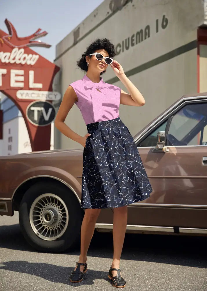A woman wearing a vintage pink dot bow neck sleeveless cotton top paired with a navy constellation print skirt