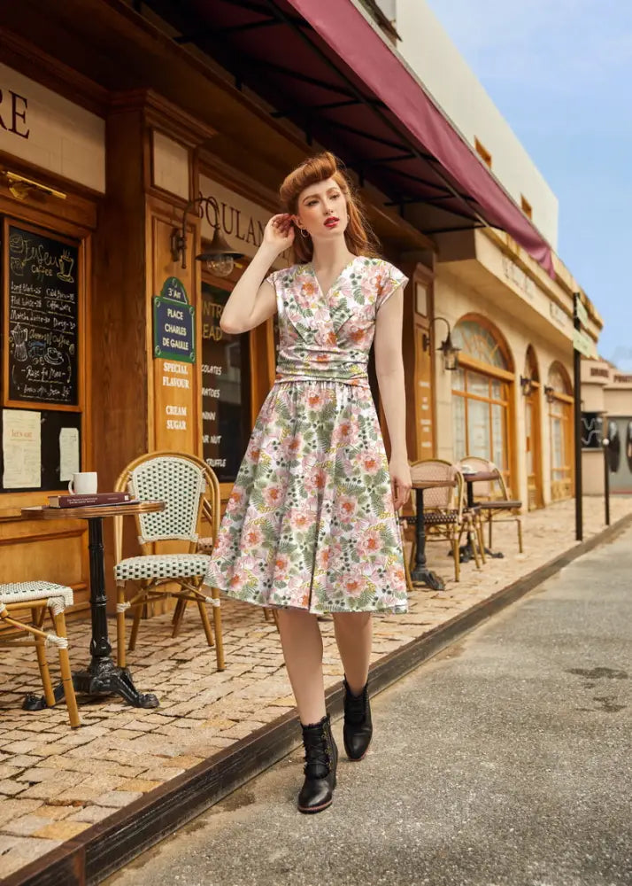 A woman wears a pink floral Greta vintage cotton knee length dress with short sleeves and a fitted waist