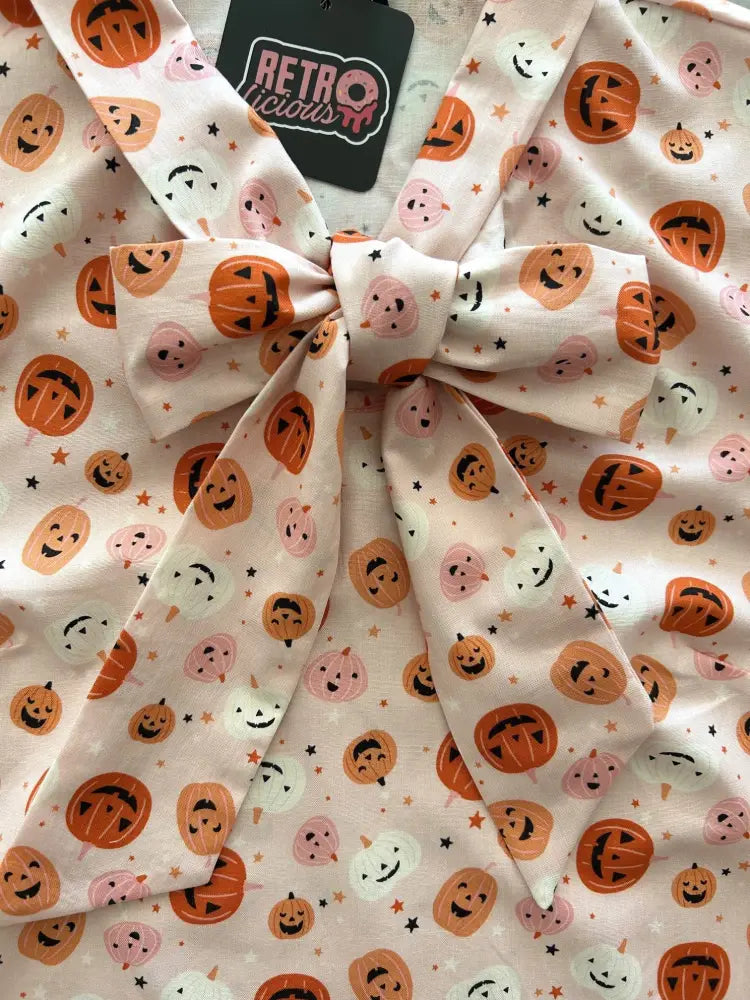 A soft off-white fabric pink jack-o-lantern vintage bow top with orange and pink smiling pumpkins and stars pattern