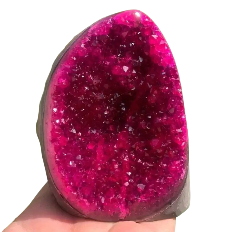 A vibrant fuchsia pink quartz geode crystal cluster with sparkling formations held against green foliage for home decor