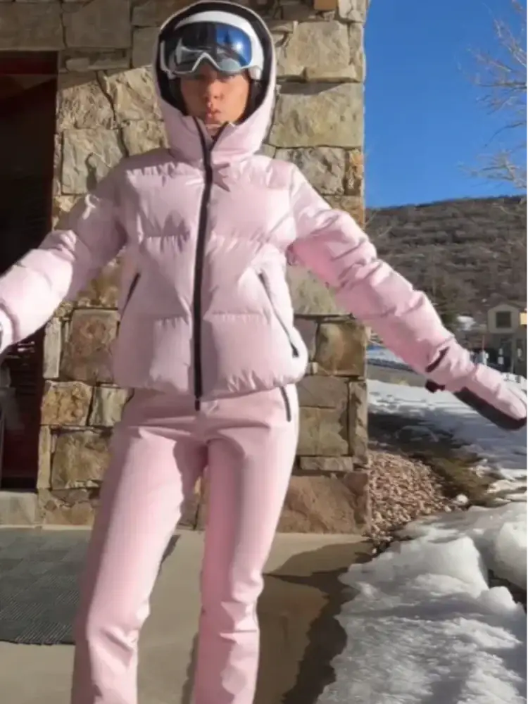 Pink waterproof women ski suit featuring a hooded design and black zipper in a puffer material for winter snowwear