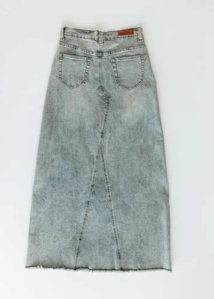 Back view of piper light wash a-line denim maxi skirt featuring a frayed hem and back pockets in light-wash denim