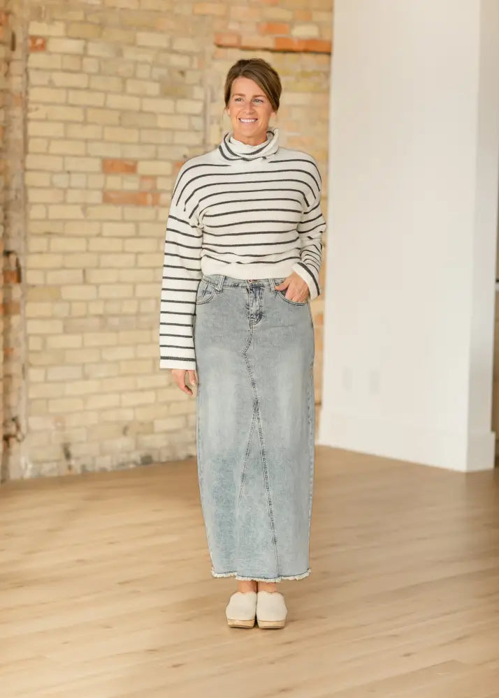A woman wears a piper light wash a-line denim maxi skirt with front seam and frayed hem made of light-wash denim