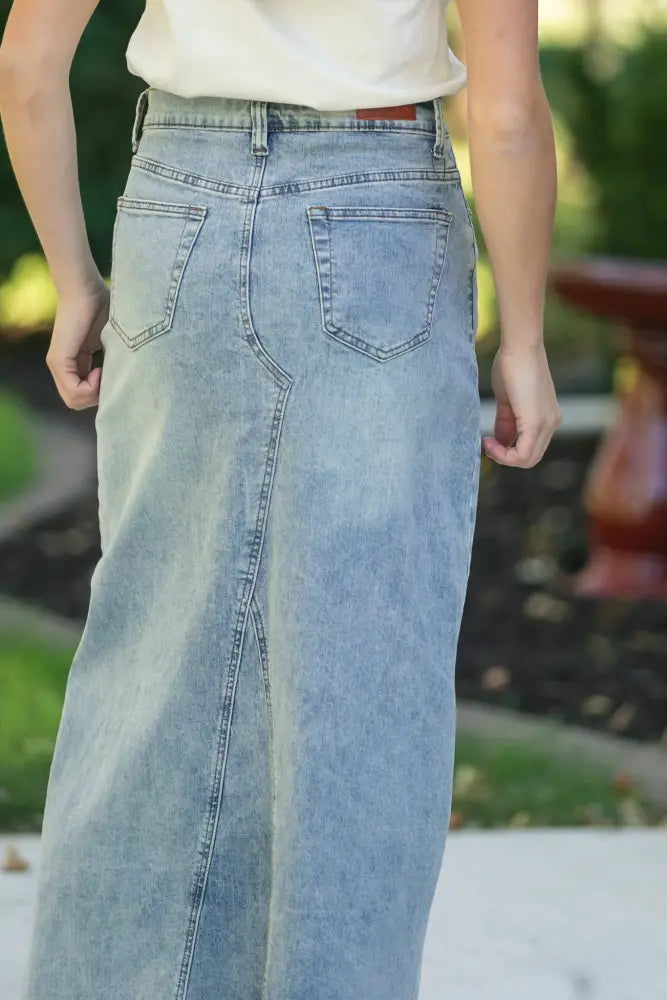 Back view of piper light wash a-line denim maxi skirt with high waist two back pockets and frayed hem