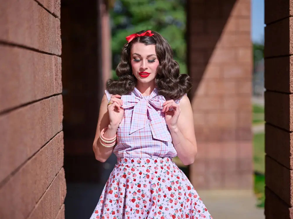A woman wears a vintage pink plaid sleeveless blouse with a large bow at the neckline and bust darts