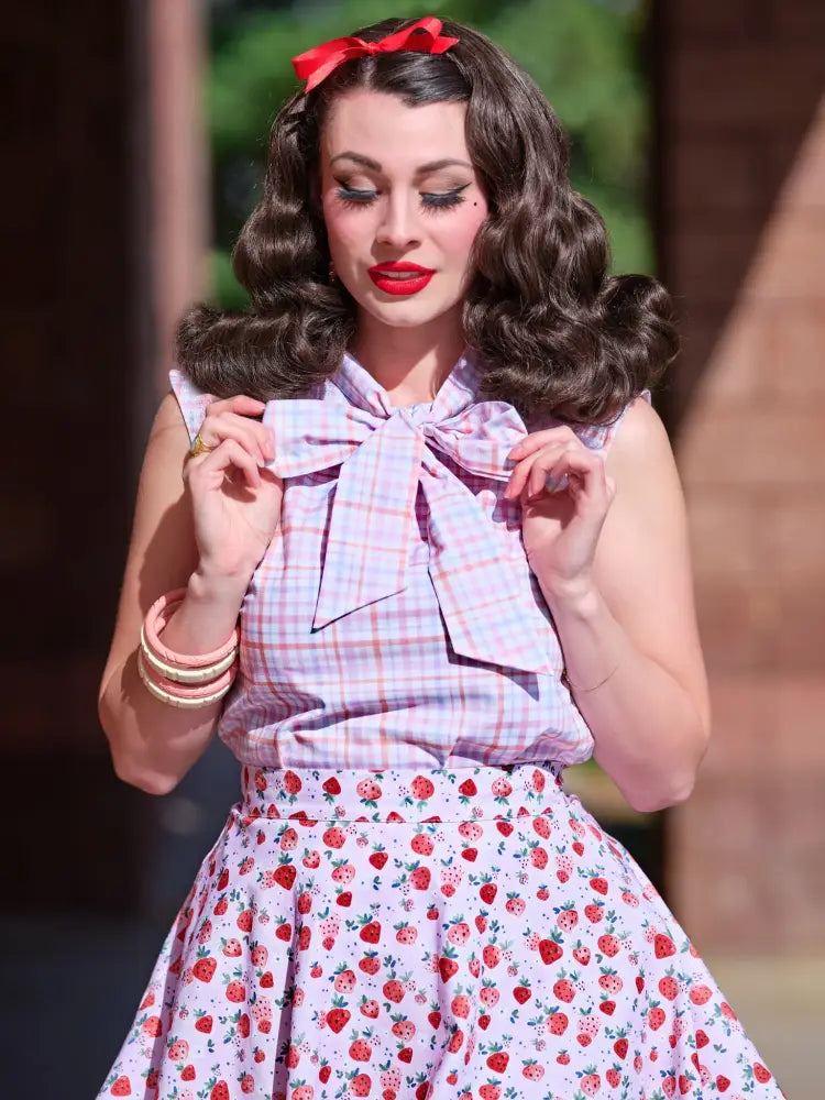 A woman wears a vintage pink plaid sleeveless blouse with a large bow at the neckline and bust darts