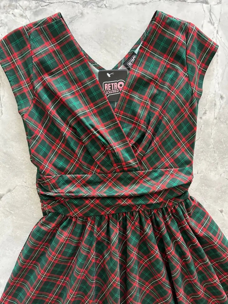 A festive green and red plaid cotton a-line dress with v-neckline, short sleeves, cinched waist, and pockets