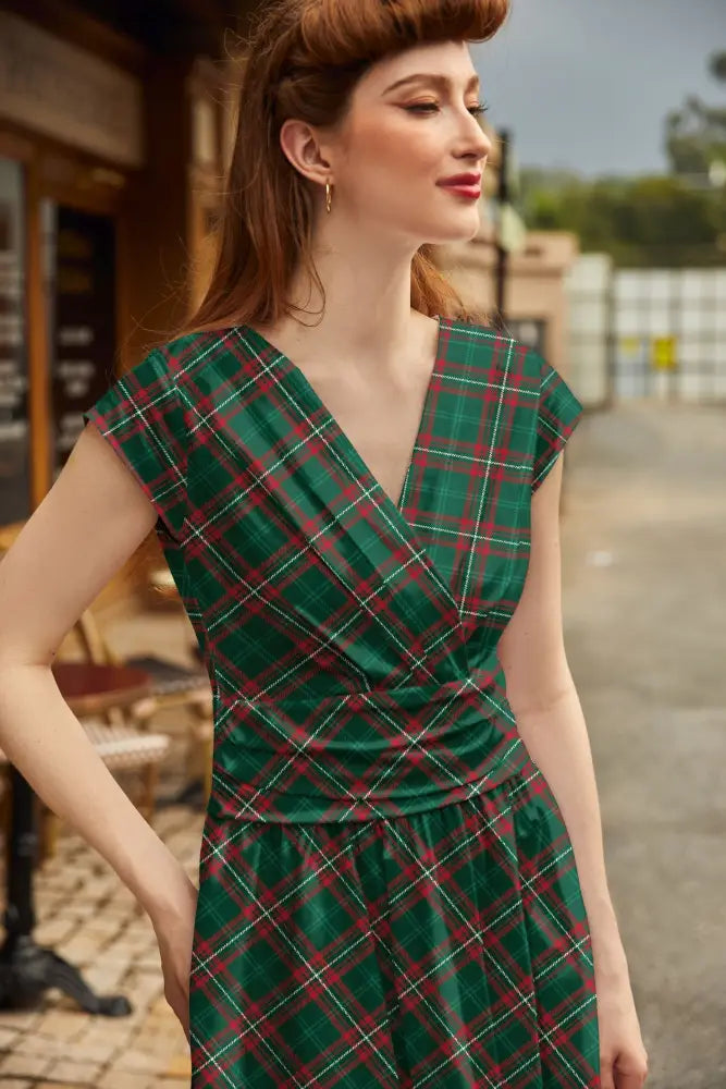 A woman wearing a green and red plaid Greta plaid v neck cotton a line dress with short sleeves and pockets
