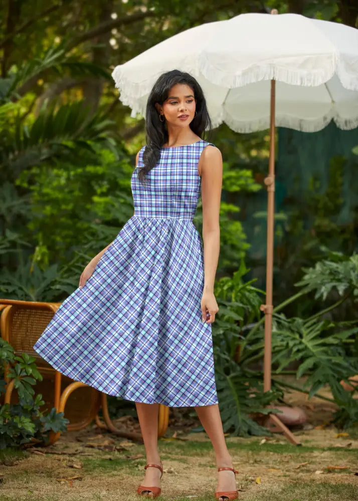A woman wears a sleeveless blue and cream plaid 1950s cotton midi swing dress with an a-line silhouette