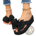 Black platform flip flops with large sheer ruffled bow accents made of lightweight fabric for stylish wear