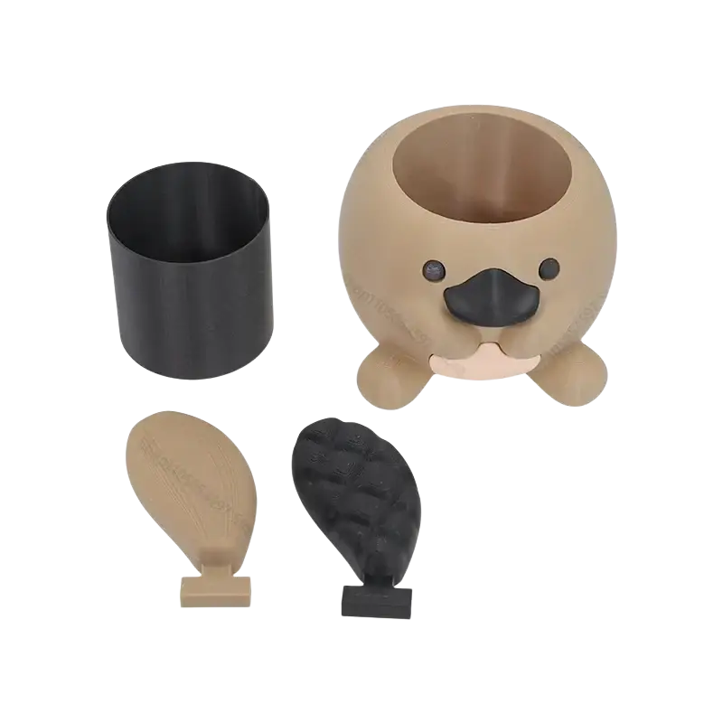 Beige and black plastic platypus-shaped toothbrush holder with rounded body, small feet, and textured snout for desk use