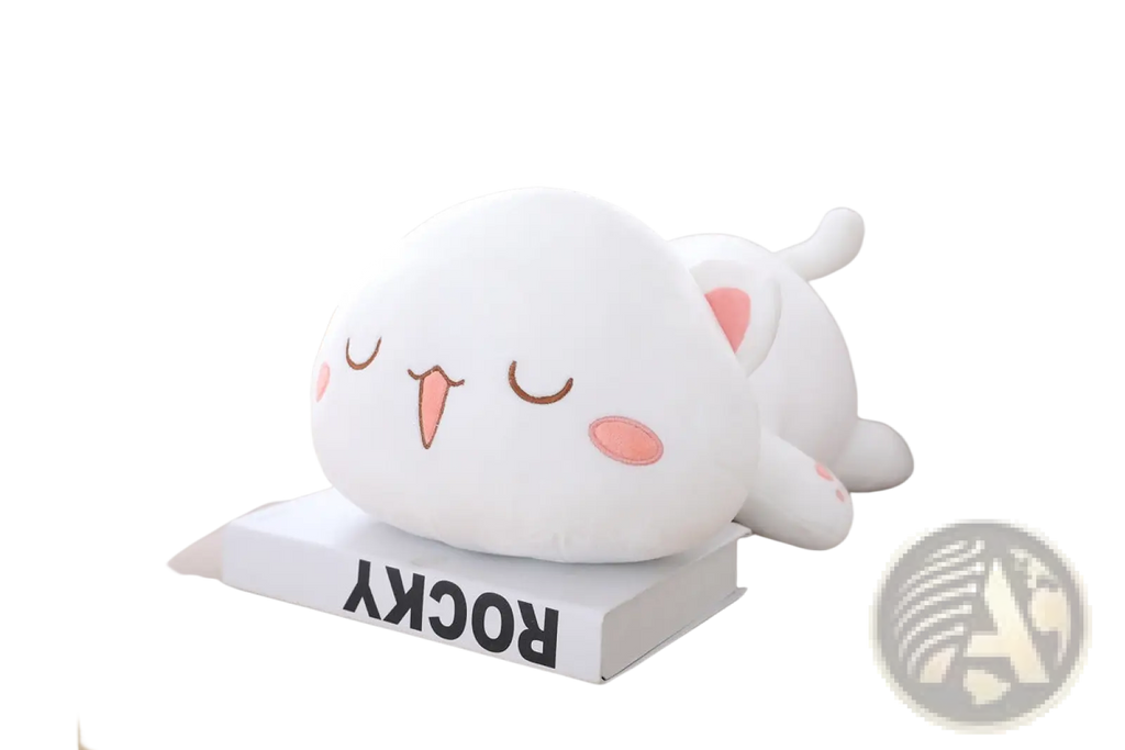A plush white cat pillow doll with pink inner ears cheeks and tongue lying on its side on a book soft kitten toy