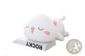 A plush white cat pillow doll with pink inner ears cheeks and tongue lying on its side on a book soft kitten toy