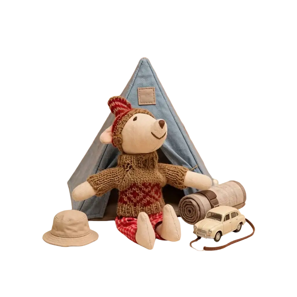 A plush mouse doll stuffed animal toy wearing a red and brown knitted sweater hat and patterned pants seated by a denim tent