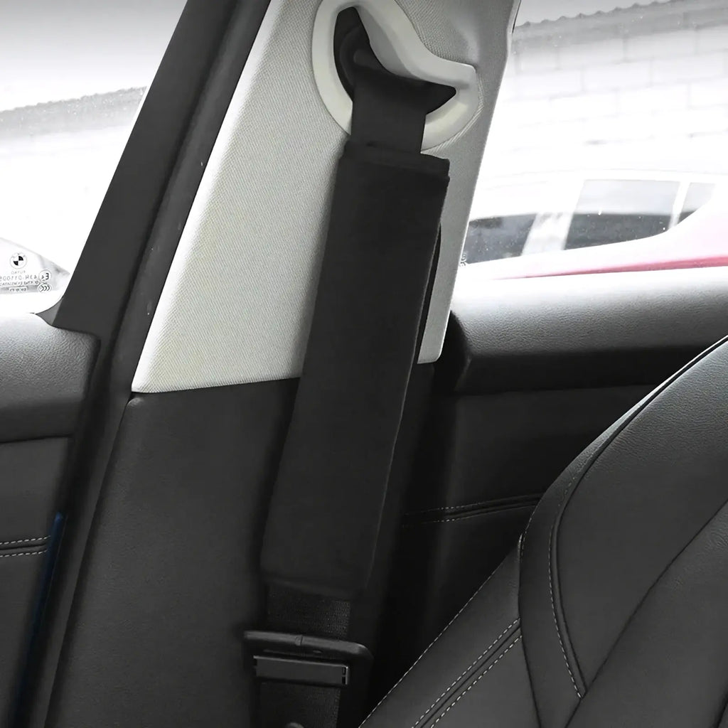 Plush seat belt cover in black fabric with padded design and white plastic buckle attachment for car shoulder pads