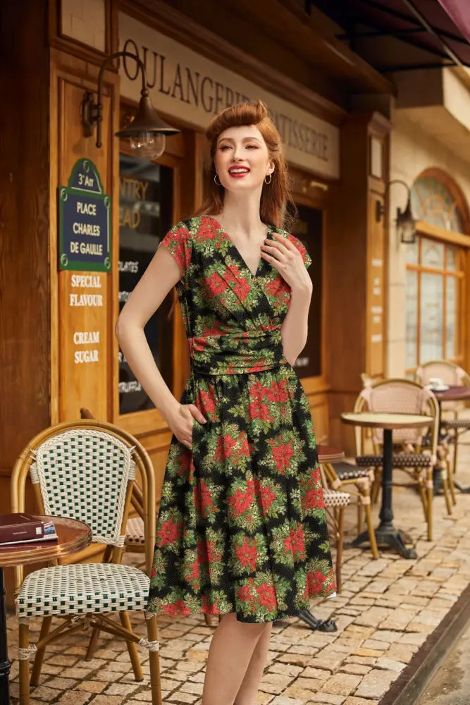 A woman wears a poinsettia greta vintage floral cotton midi dress with pockets featuring red flowers on black