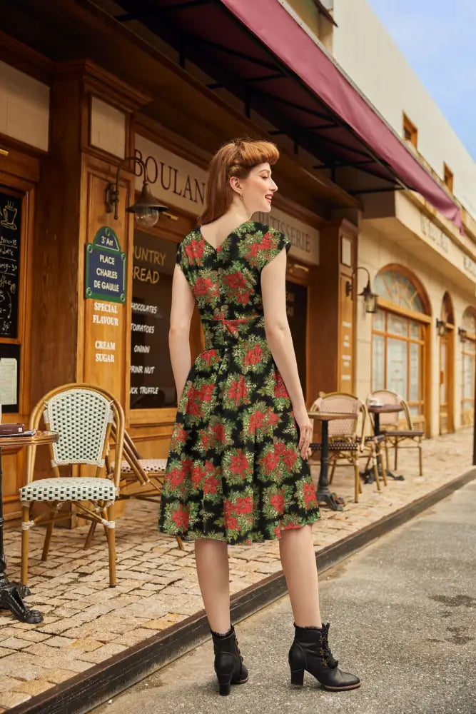 A woman wears a poinsettia greta vintage floral cotton midi dress with pockets in black with red floral patterns